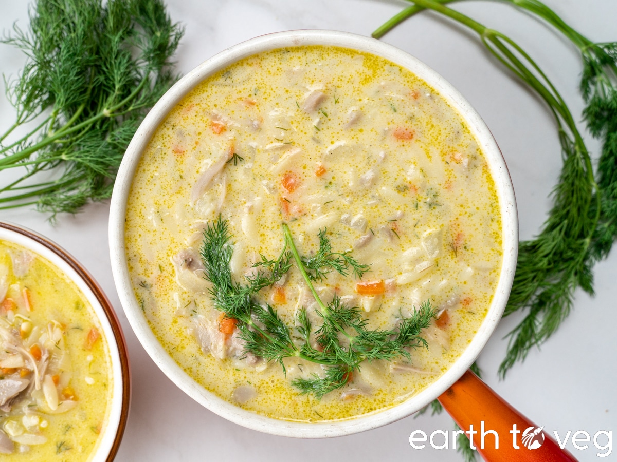 small stockpot full of vegan avgolemono lemon rice soup, garnished with dill, with another bowl off to the side