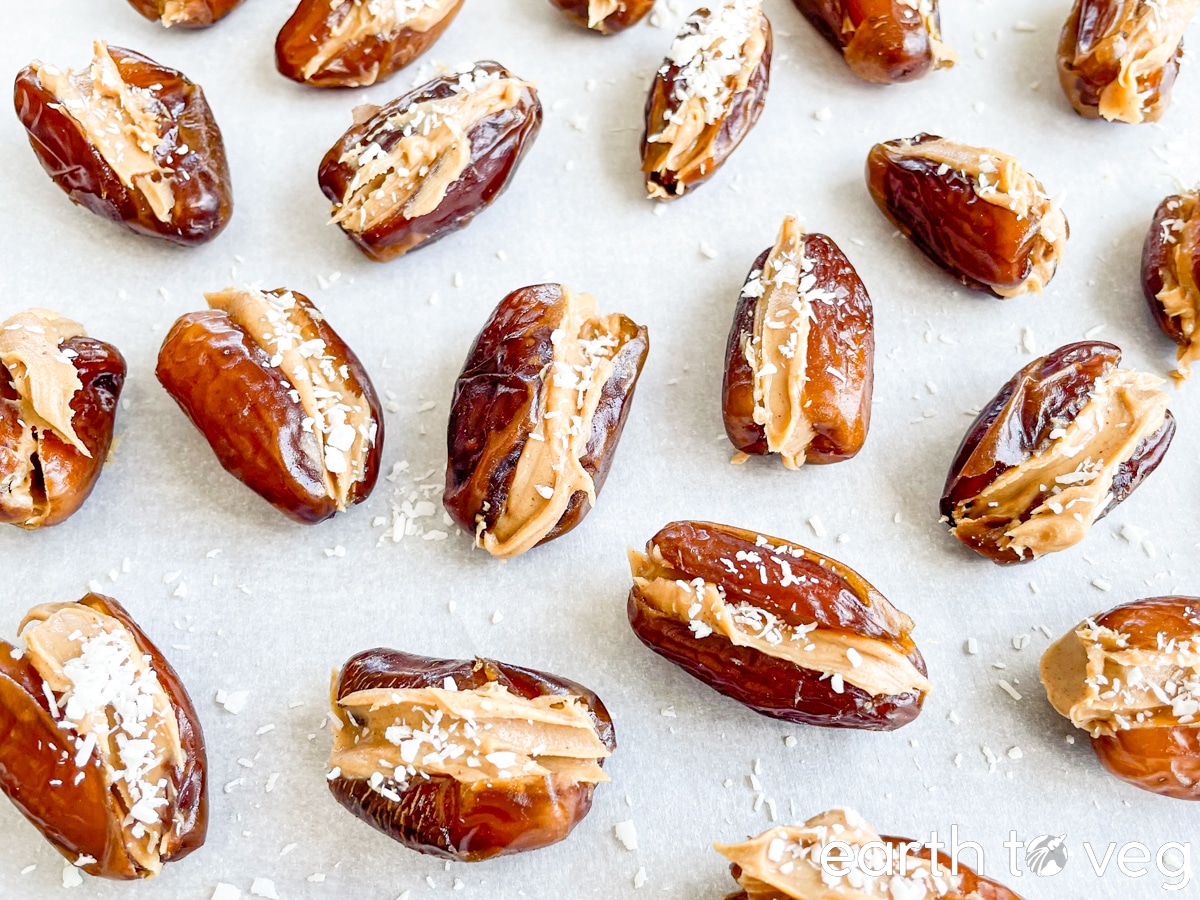 Peanut butter stuffed dates scattered with shredded coconut on a sheet of parchment paper.